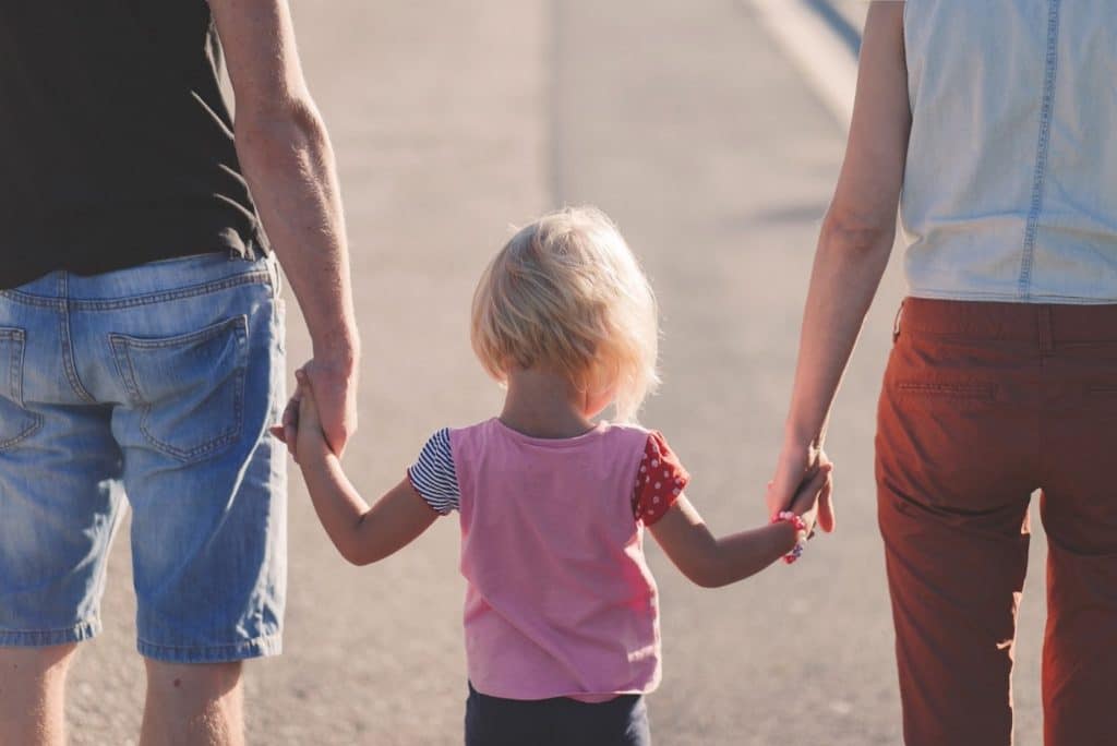 A child holding the hands of both her parents.